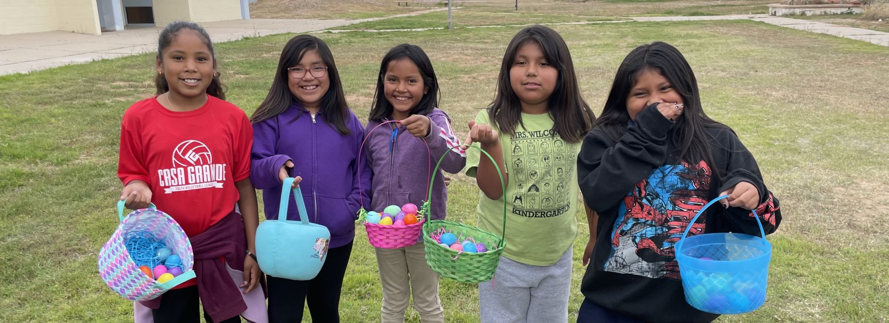 Five students standing outside Santa Rosa Day School happily holding easter baskets.