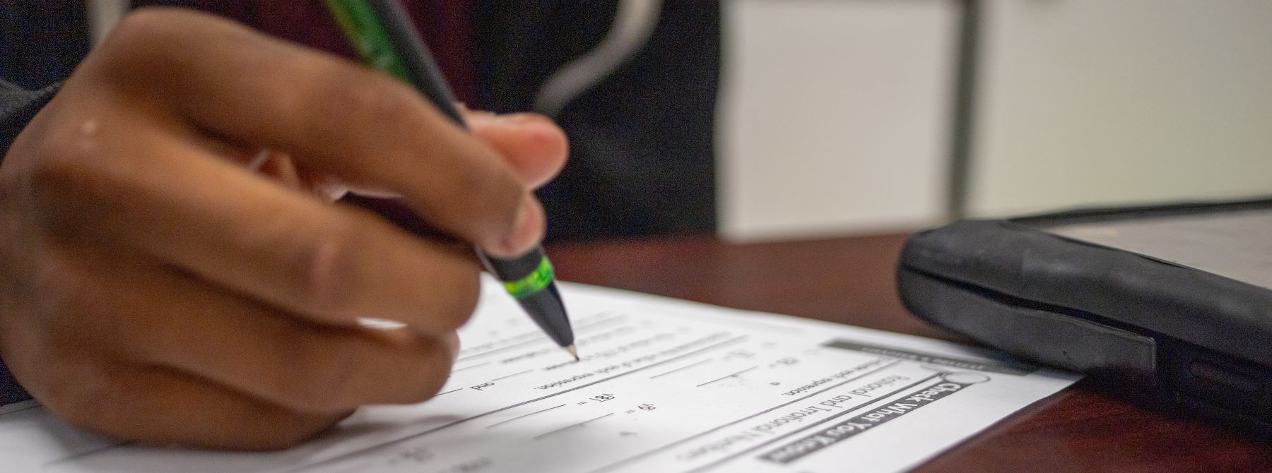 A person writes on a piece of paper with a pen, focused on their task.