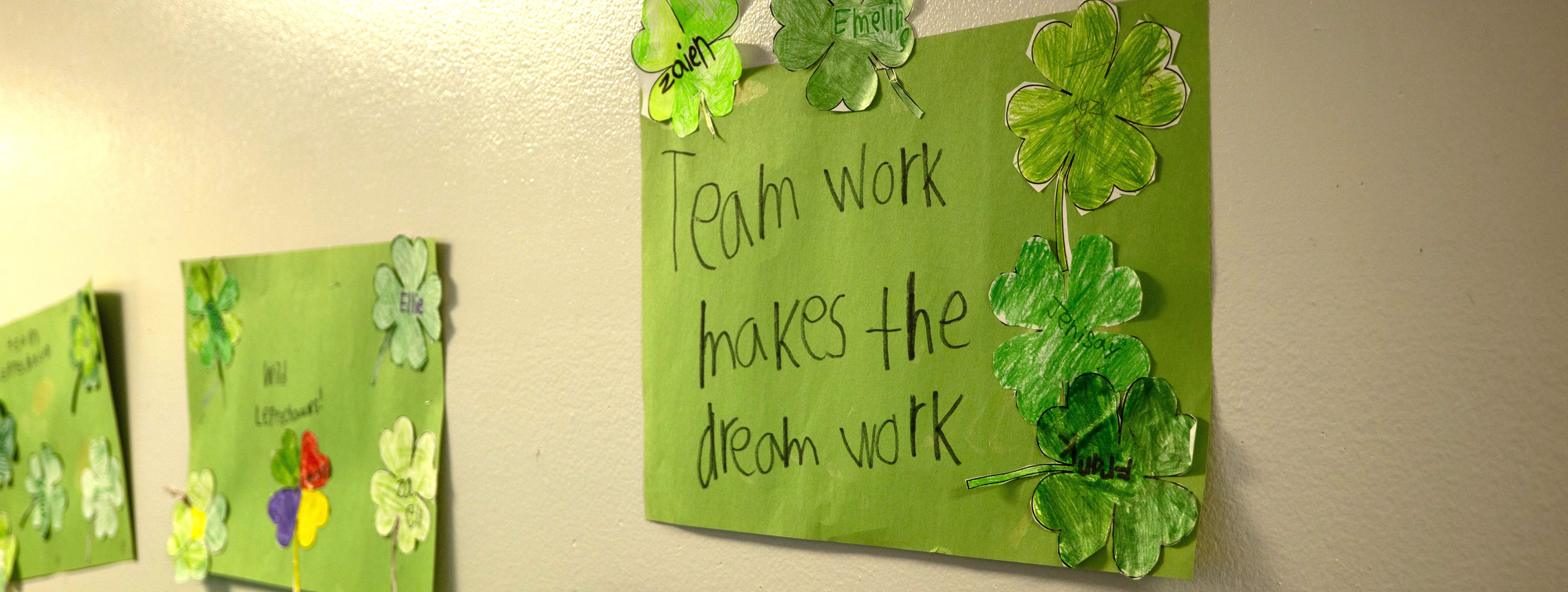 Green paper shamrocks on a wall featuring the phrase "team work makes the dream work".